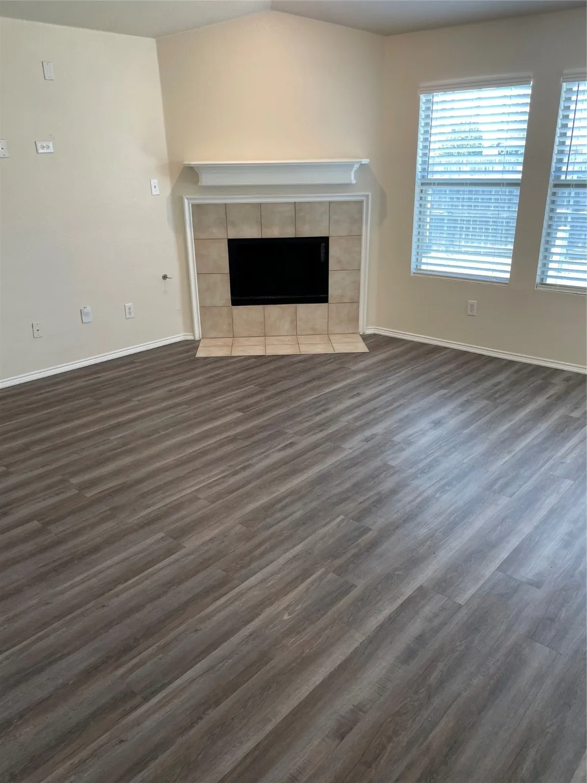 Unfurnished living room featuring a tile fireplace, vaulted ceiling, and dark wood-type flooring