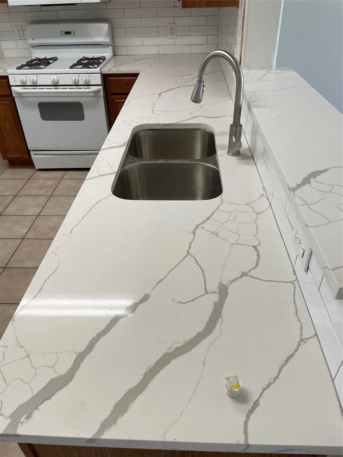 Kitchen with light stone counters, light tile patterned floors, sink, backsplash, and range