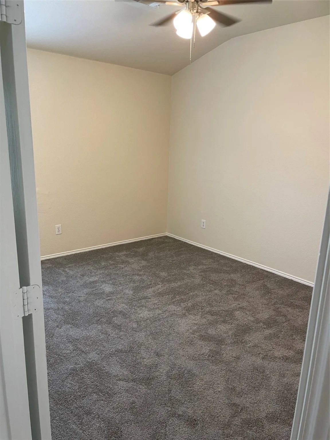 Spare room with ceiling fan, vaulted ceiling, and dark colored carpet