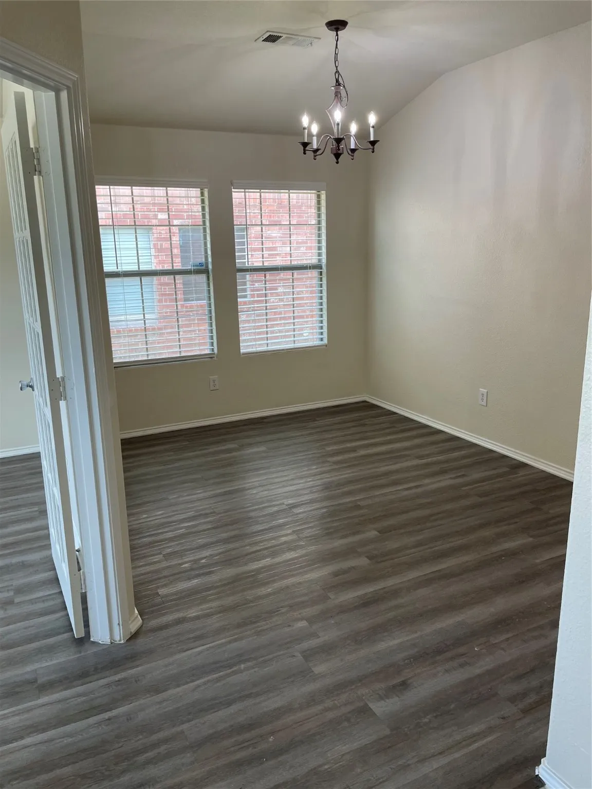 Spare room with an inviting chandelier, dark hardwood / wood-style floors, and vaulted ceiling