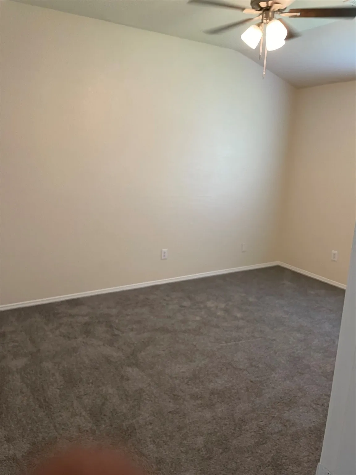 Carpeted empty room featuring ceiling fan and lofted ceiling