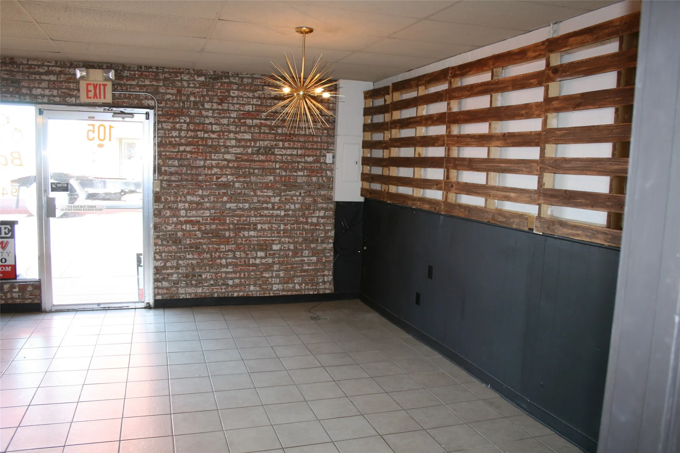 Tiled empty room featuring a paneled ceiling, an inviting chandelier, and brick wall