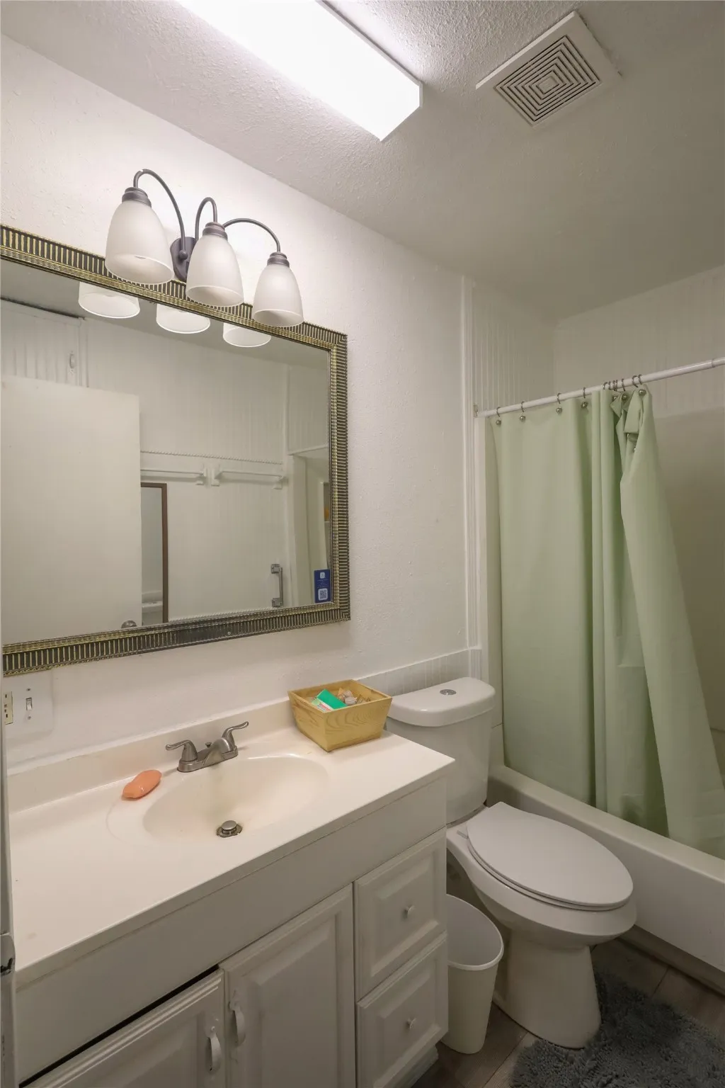 Full bathroom with vanity, a textured ceiling, shower / tub combo with curtain, and toilet
