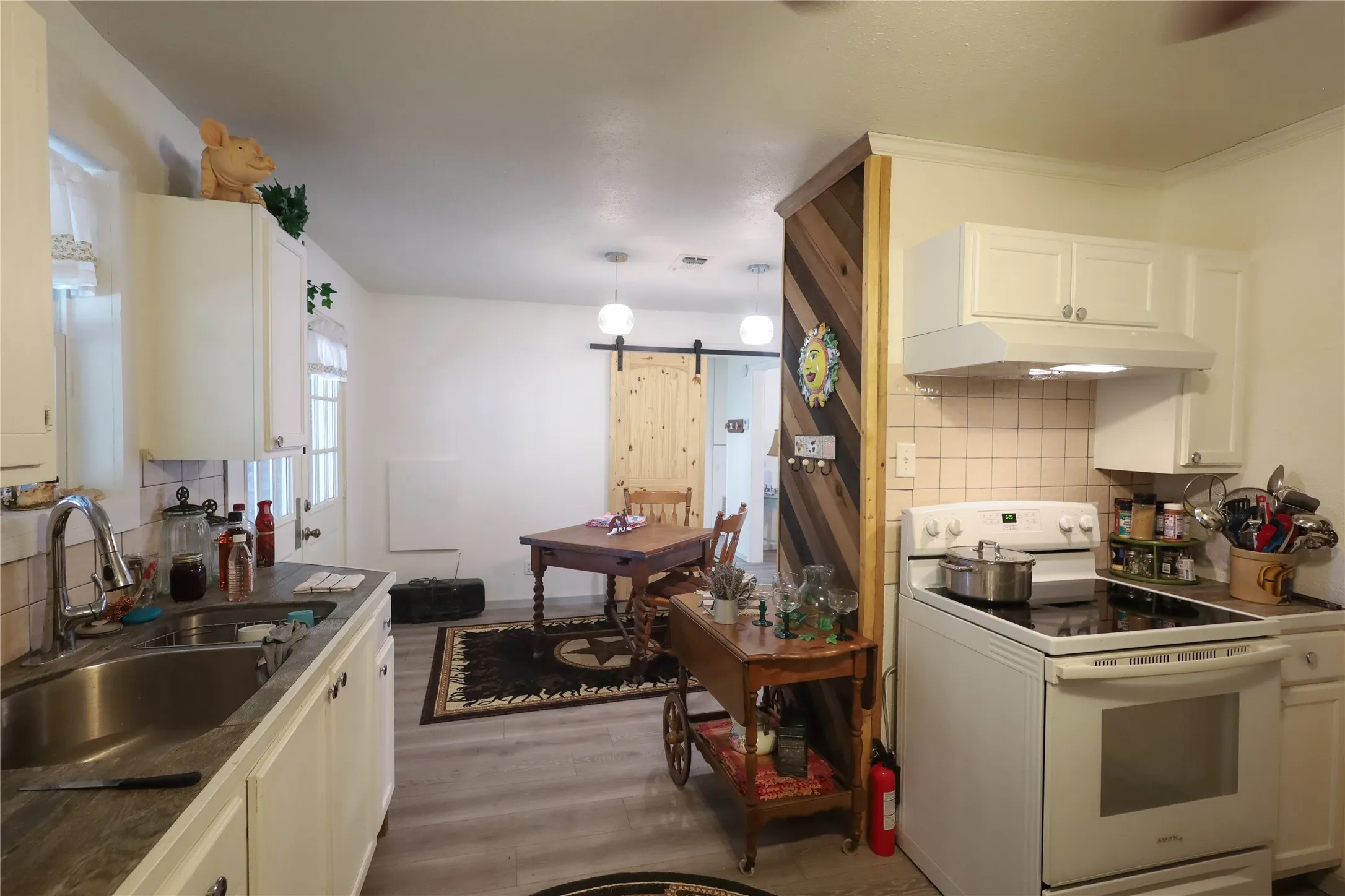 Kitchen with sink, light wood-type flooring, a barn door, white range with electric cooktop, and white cabinets