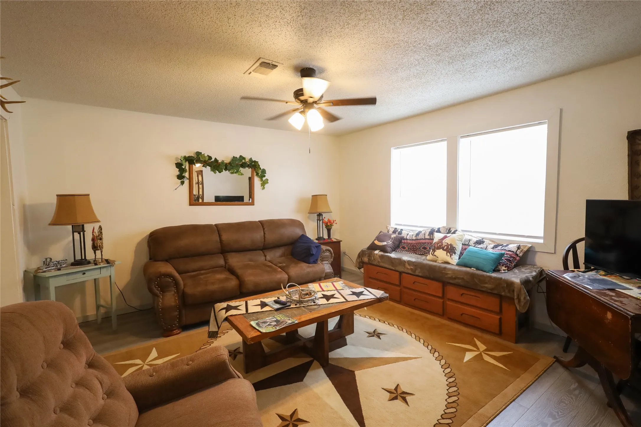 Living room with a textured ceiling, hardwood / wood-style flooring, and ceiling fan