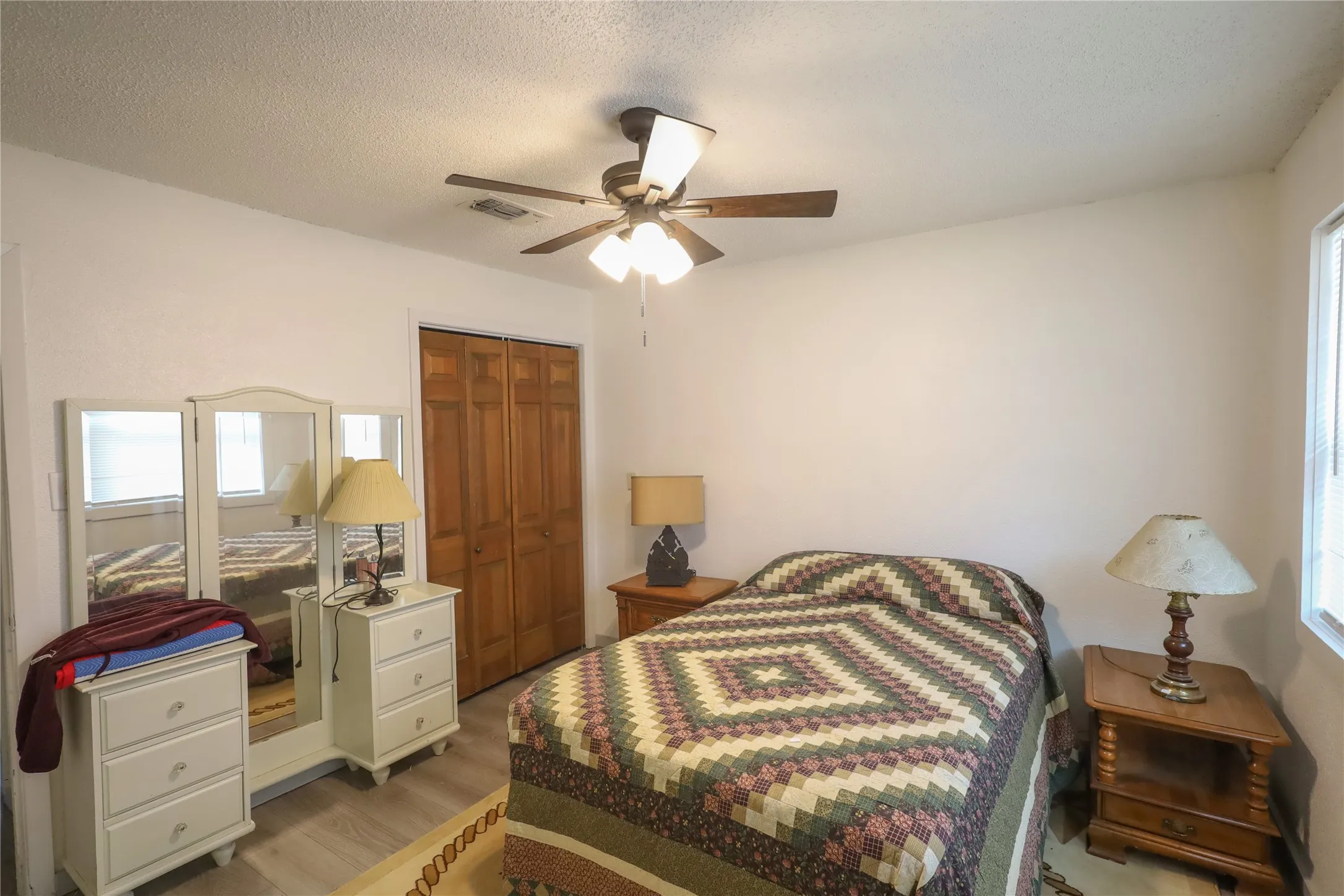 Bedroom featuring a closet, ceiling fan, a textured ceiling, and light wood-type flooring