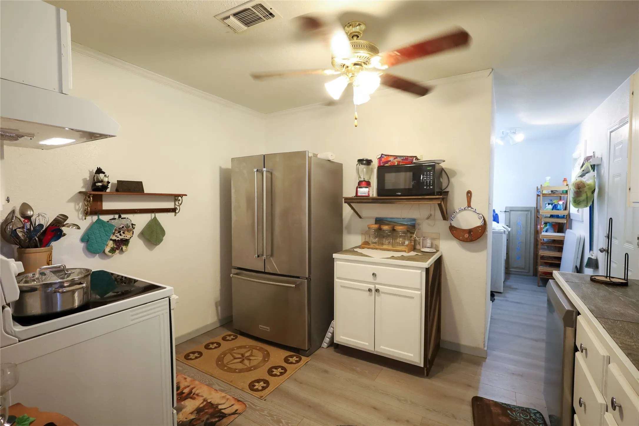 Kitchen with high end refrigerator, electric stove, white cabinetry, ornamental molding, and light hardwood / wood-style flooring