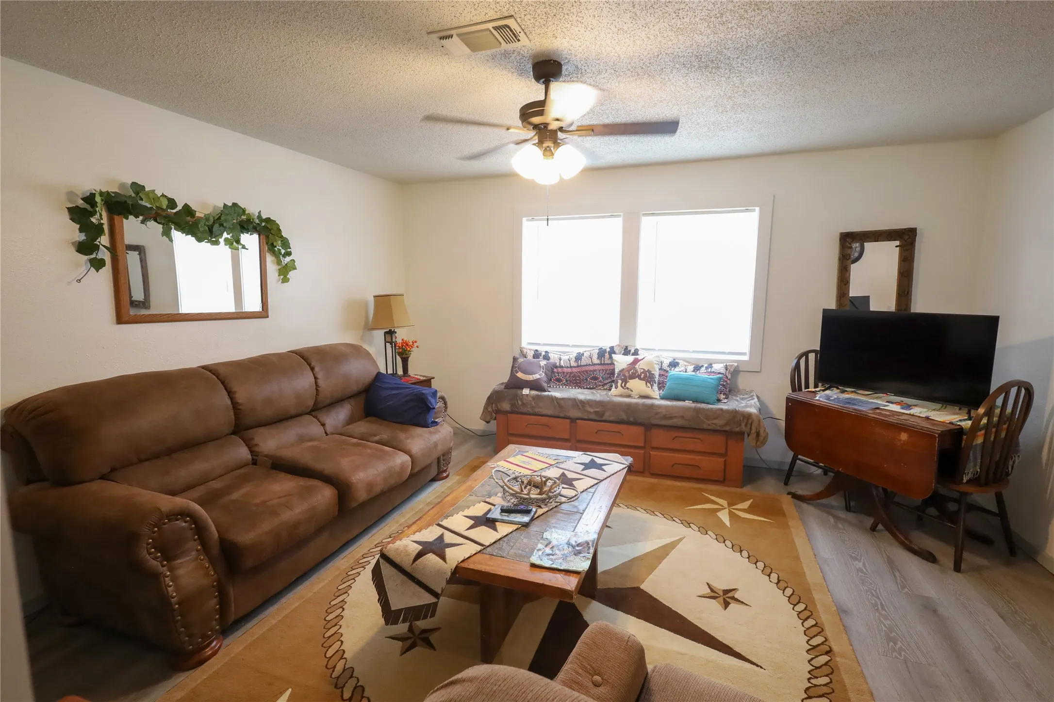 Living room with ceiling fan, a textured ceiling, and light wood-type flooring