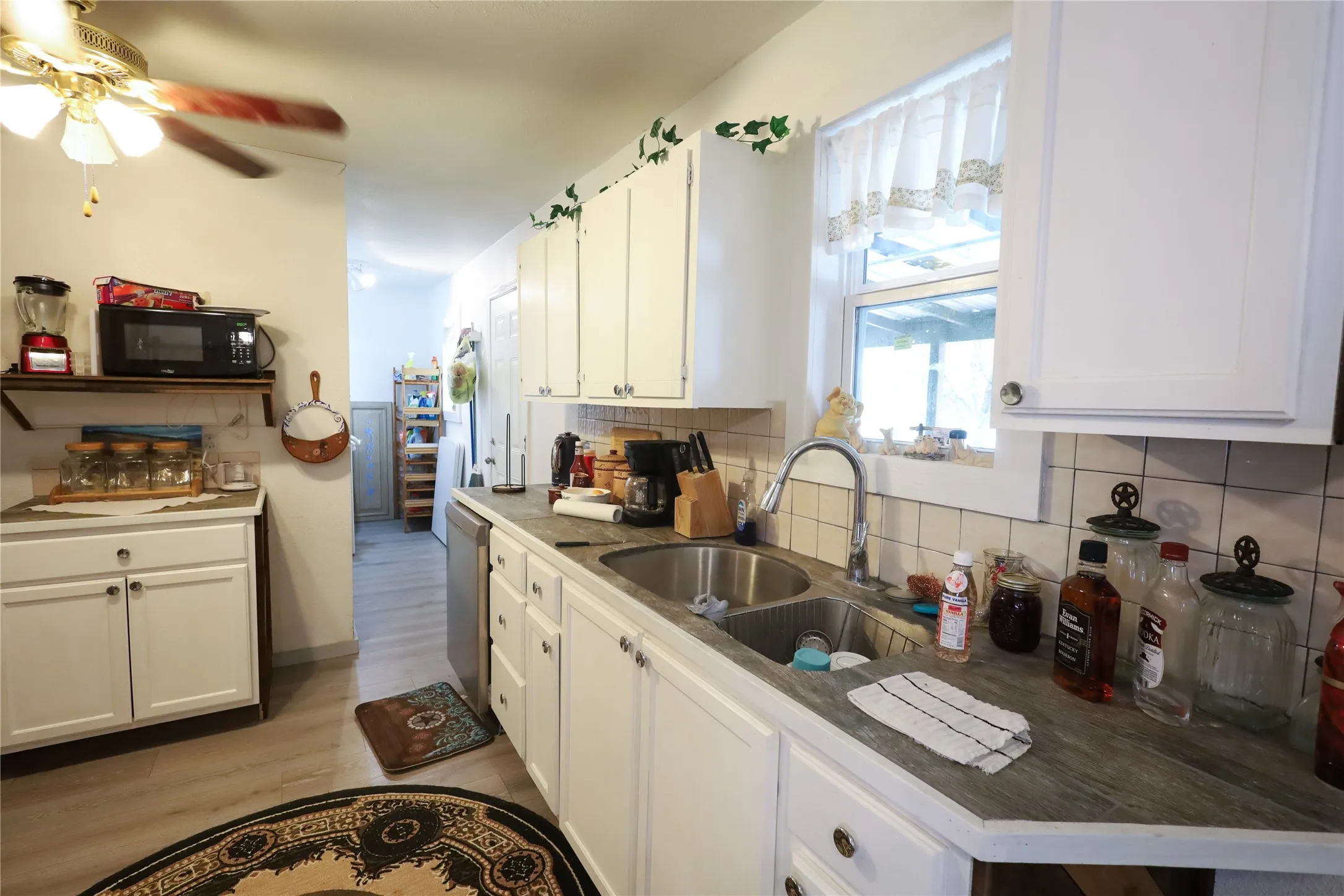 Kitchen with dishwasher, backsplash, sink, light wood-type flooring, and white cabinetry