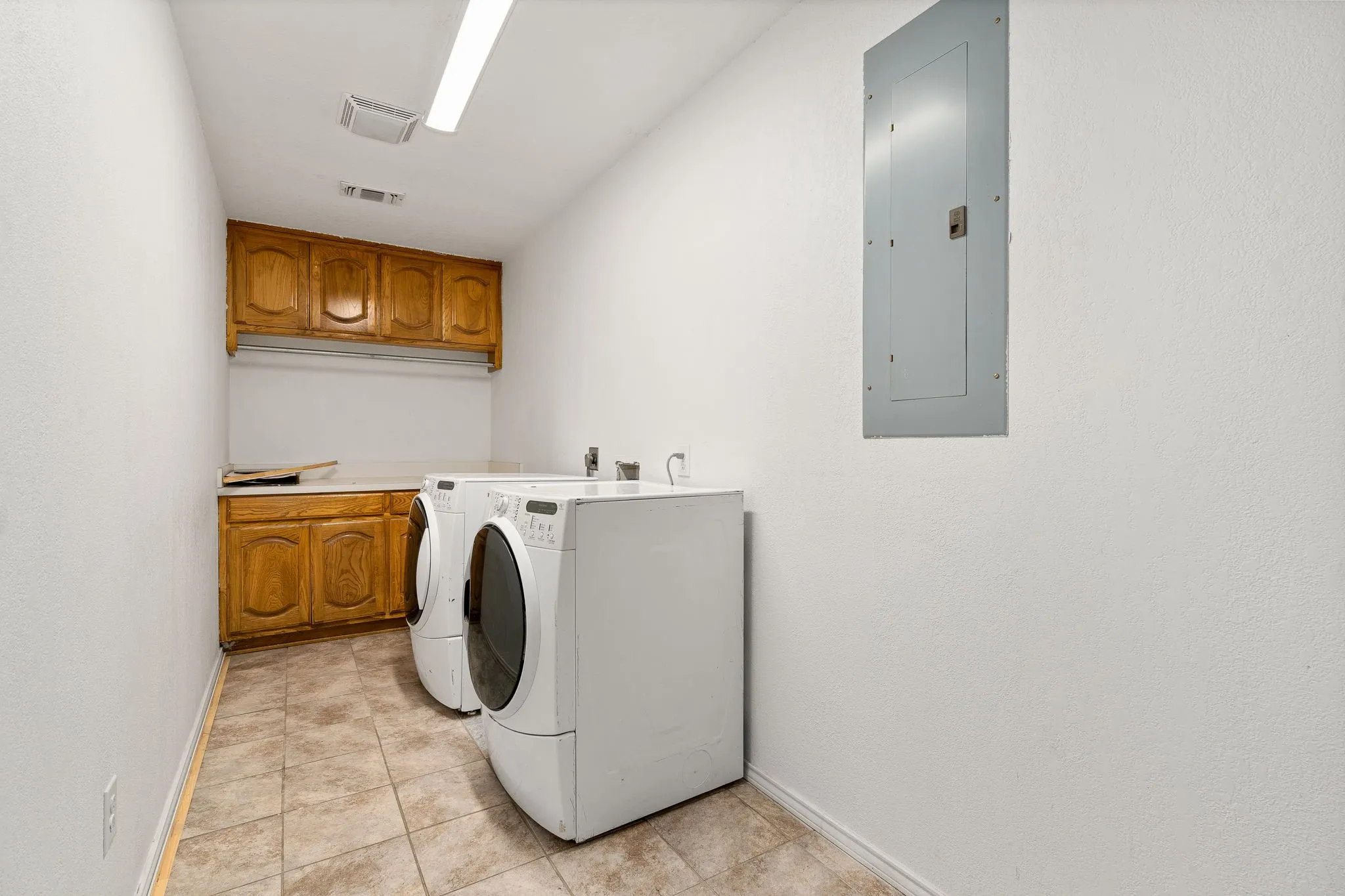 Clothes washing area featuring cabinets, electric panel, separate washer and dryer, and light tile patterned floors