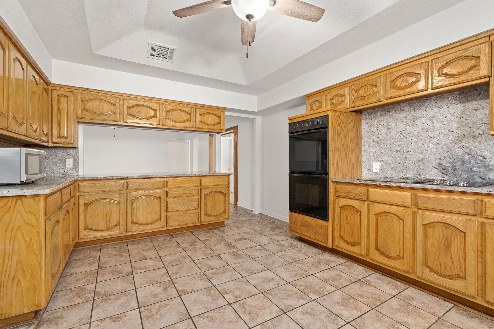 Kitchen with tasteful backsplash, ceiling fan, light tile patterned floors, a tray ceiling, and black appliances