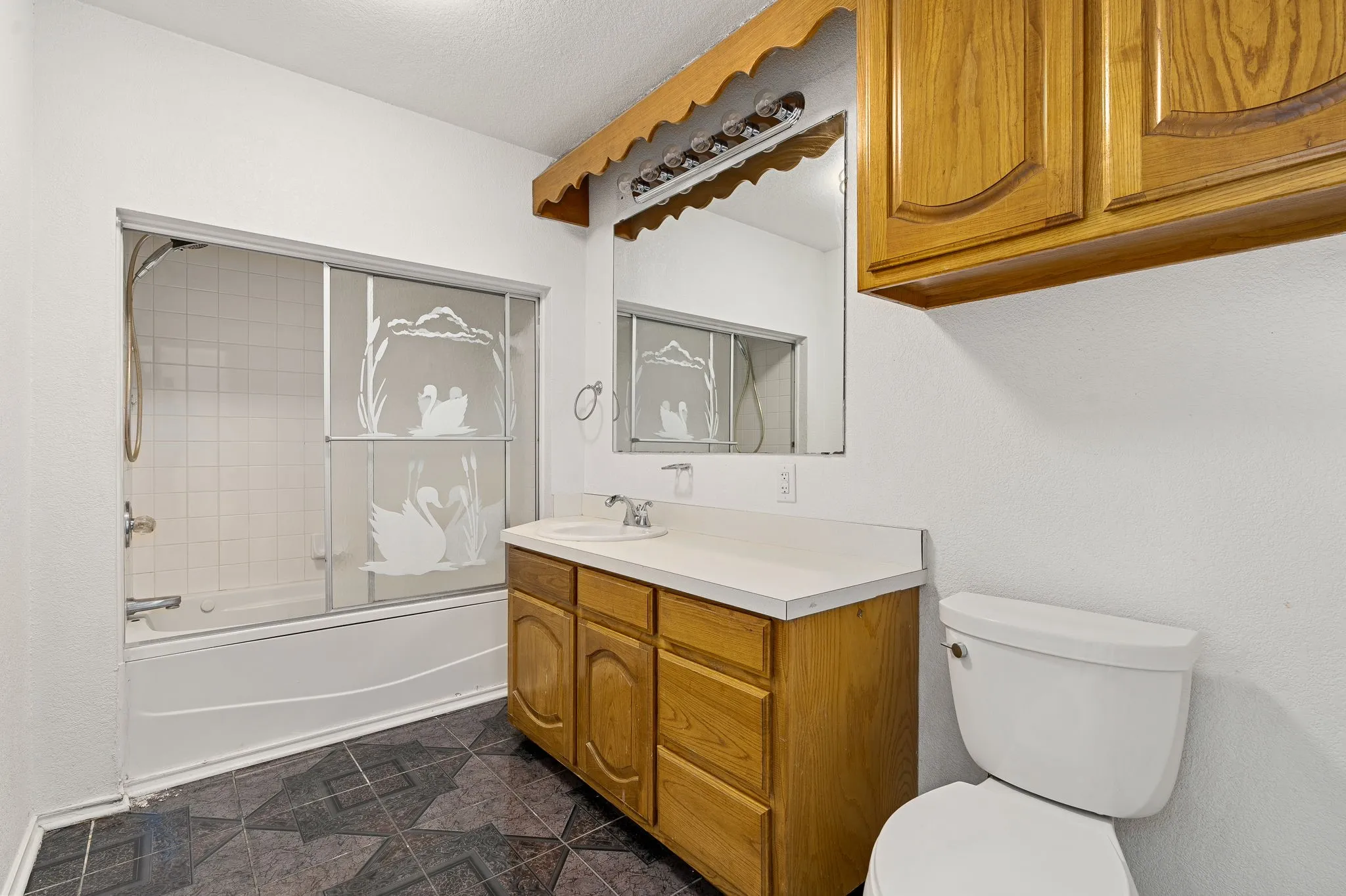Full bathroom featuring a textured ceiling, toilet, enclosed tub / shower combo, vanity, and tile patterned flooring