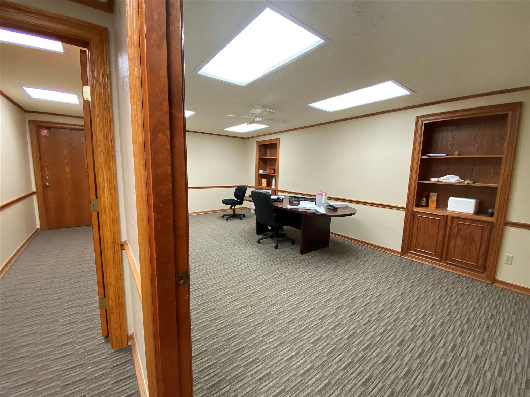 Carpeted office with built in desk and ceiling fan