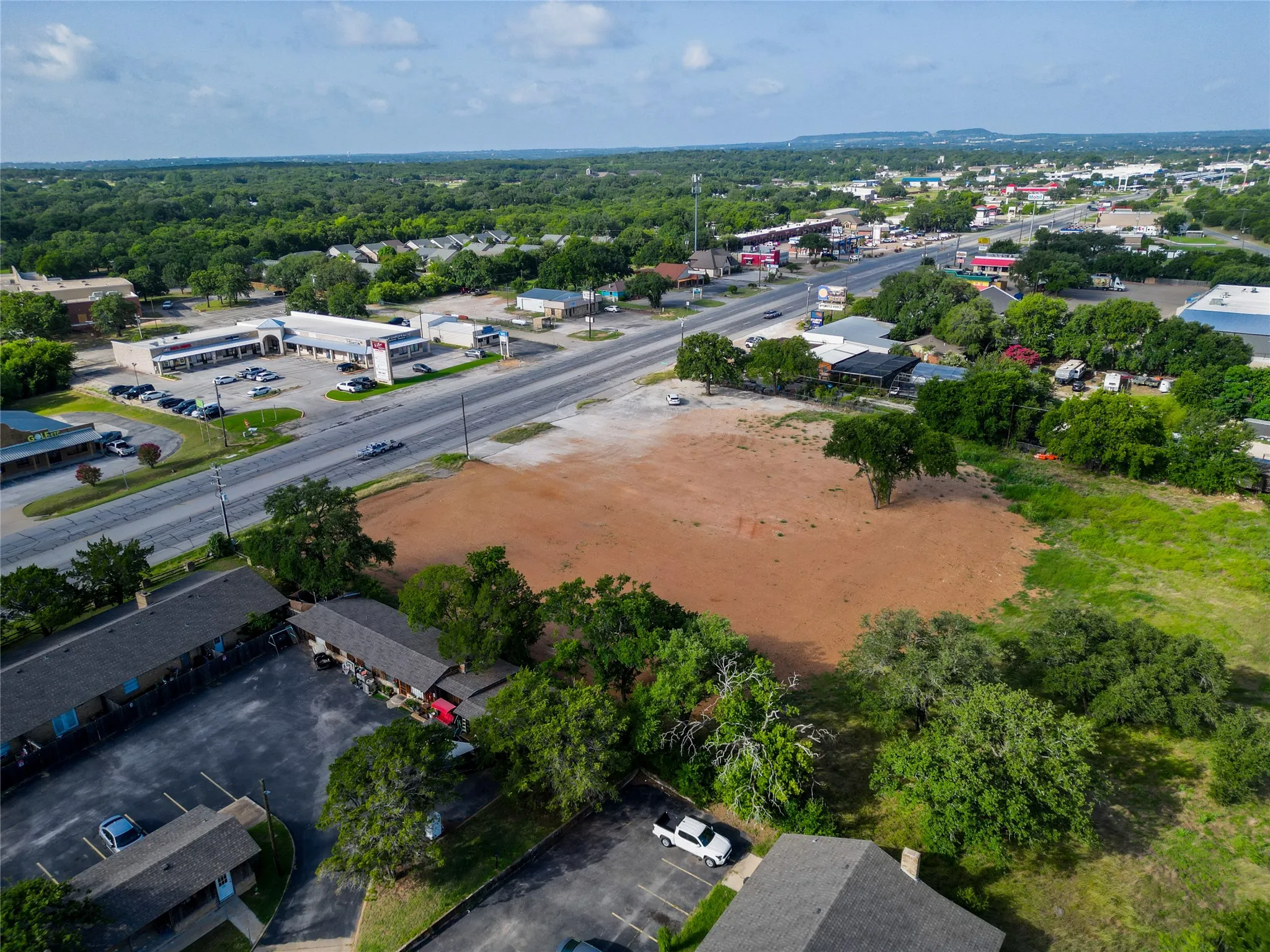 Expansive cleared lot bordered by mature trees and a paved road