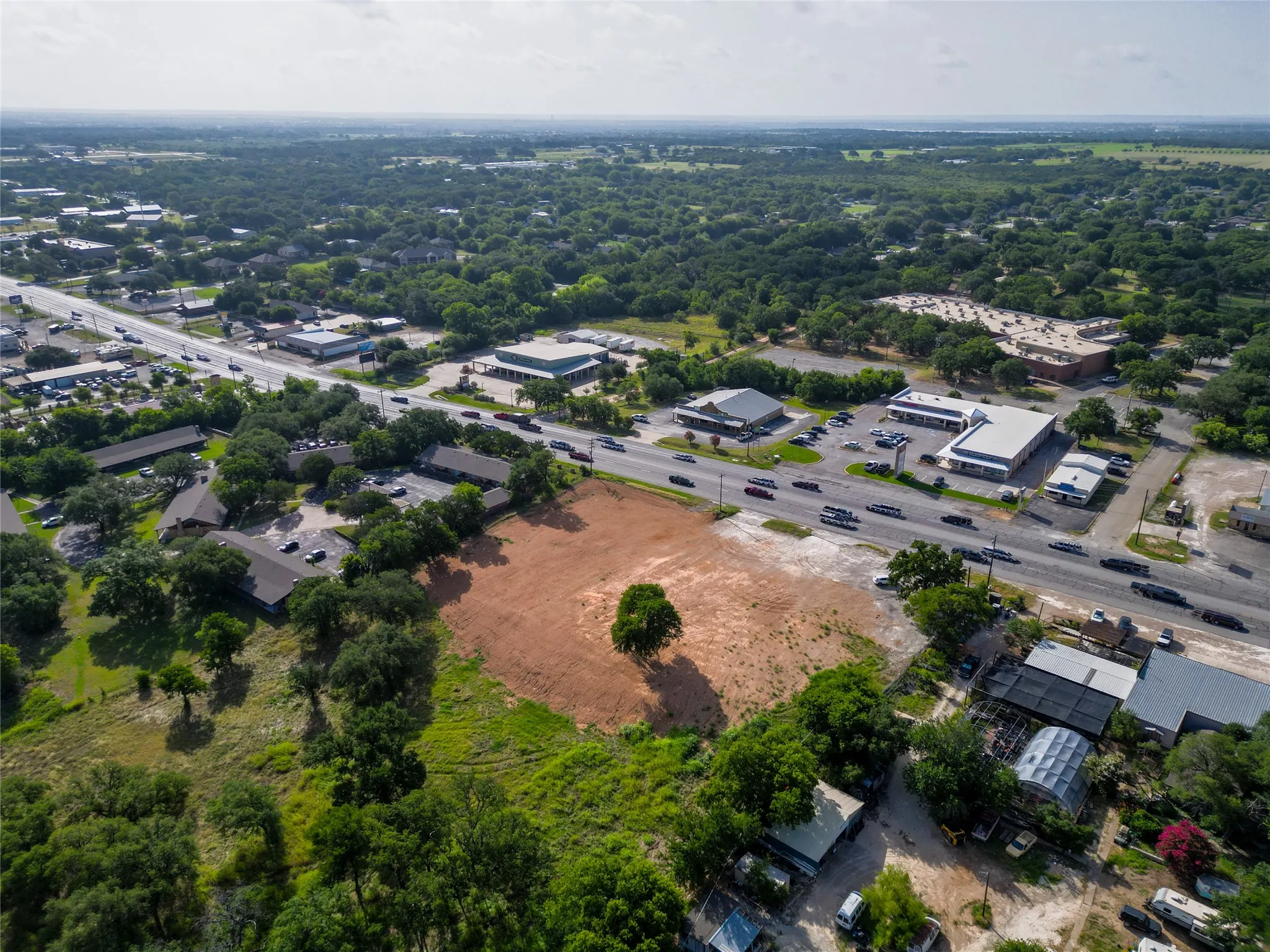 Expansive land parcel featuring cleared ground, a prominent mature tree, and direct frontage on a multi-lane road
