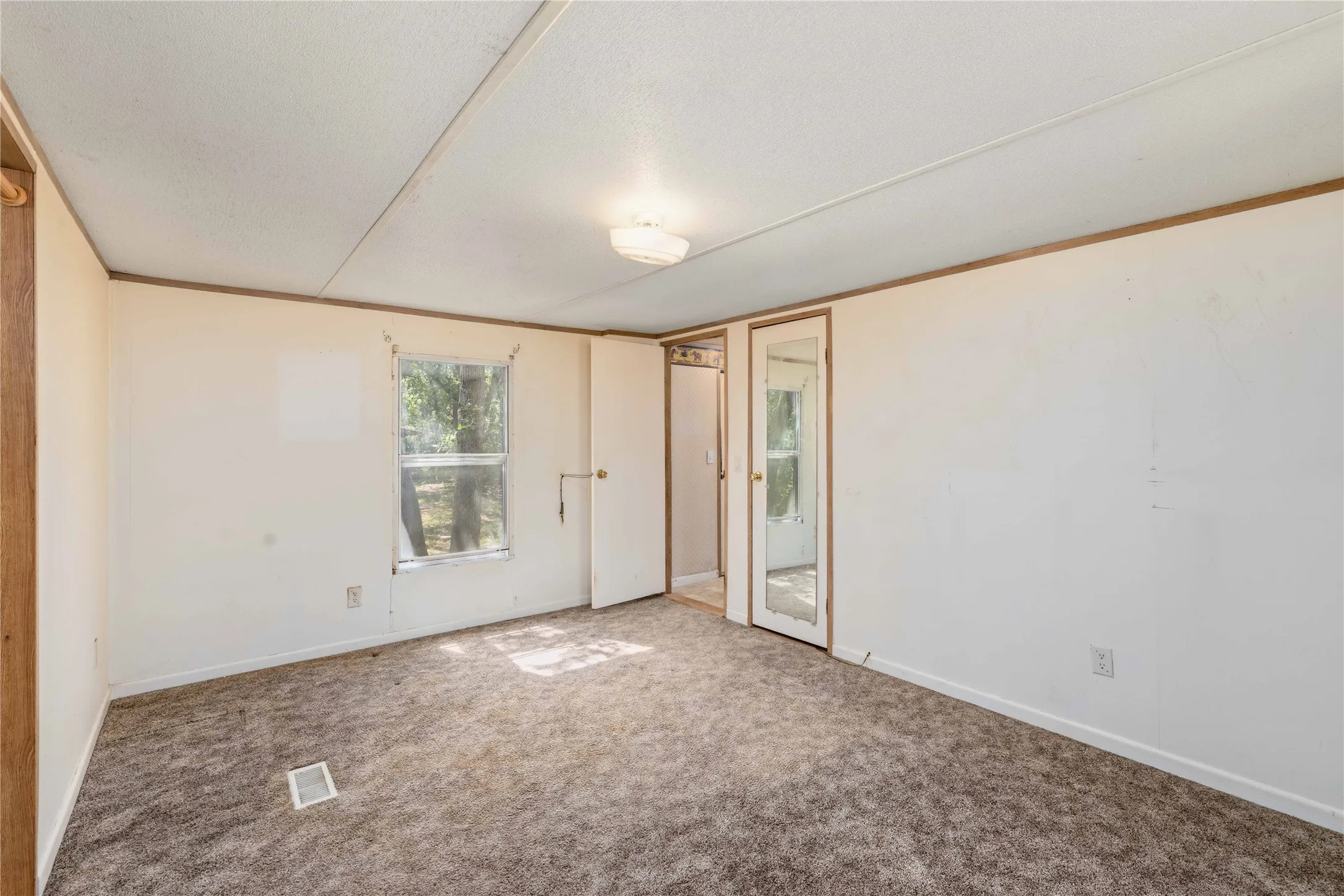 Carpeted room featuring a window with exterior views, white walls, and a ceiling-mounted light fixture