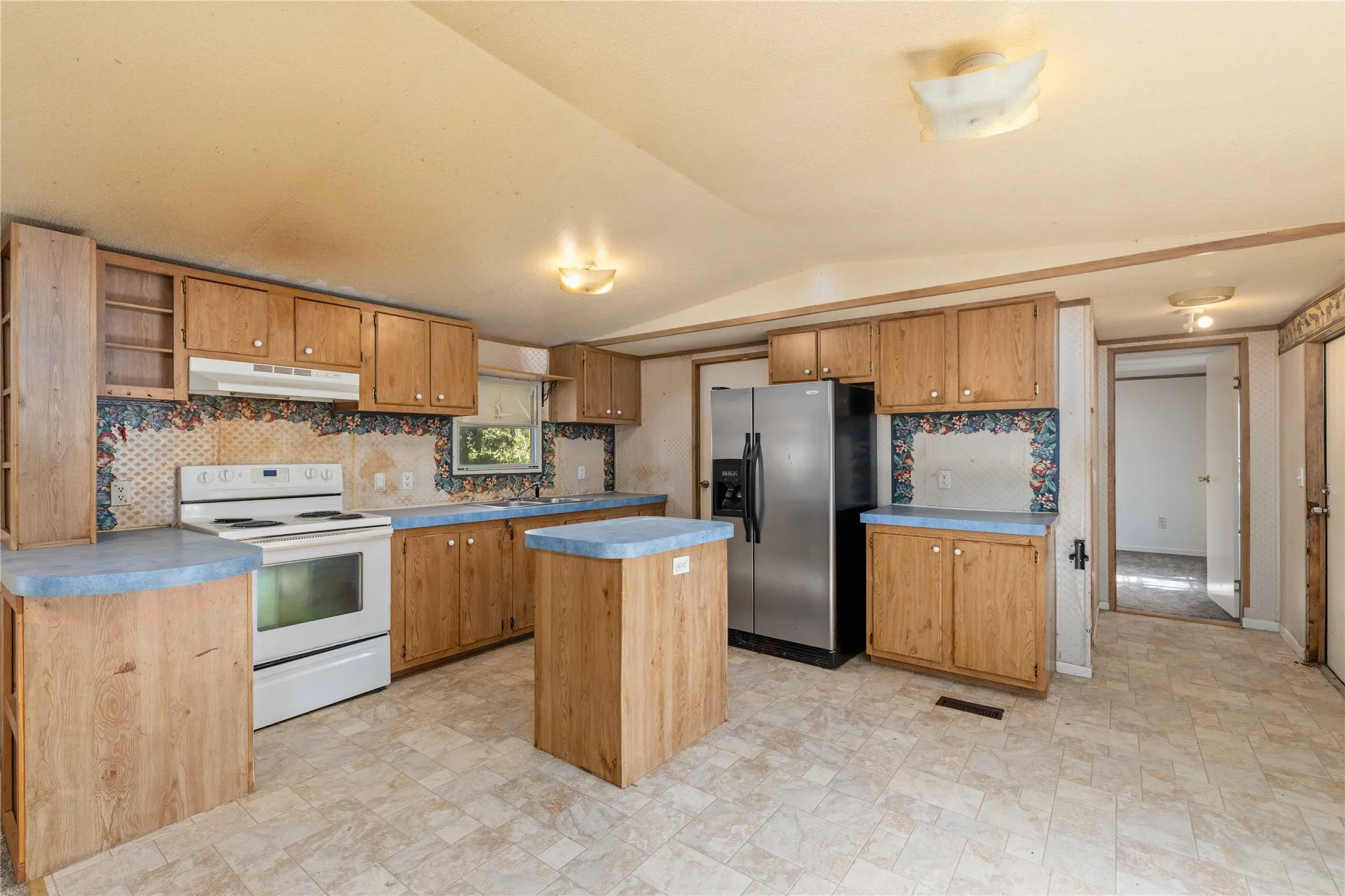 Kitchen featuring light wood-finish cabinetry, blue countertops, white electric range, and a stainless steel refrigerator