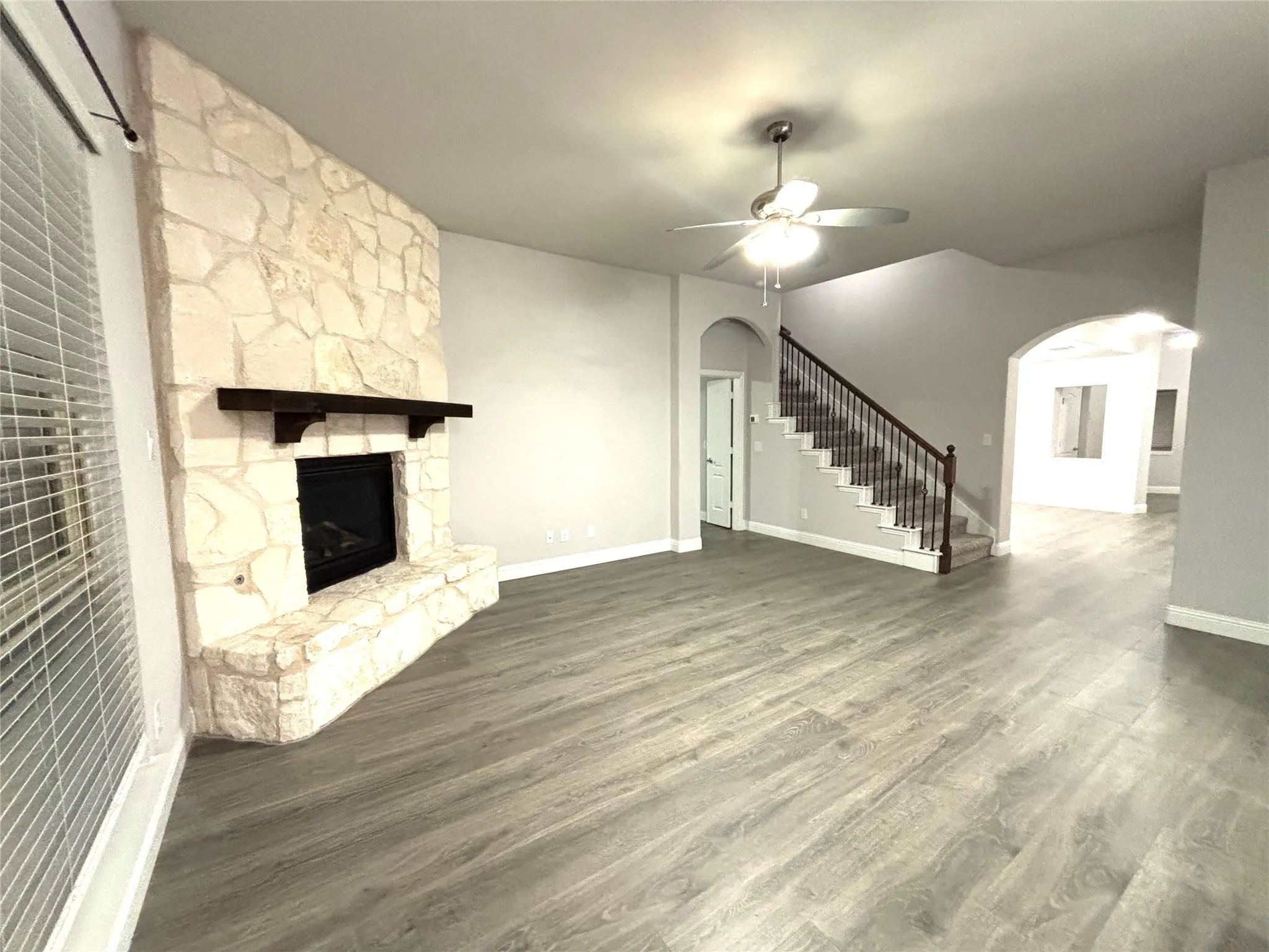 Unfurnished living room with dark hardwood / wood-style floors, ceiling fan, and a stone fireplace