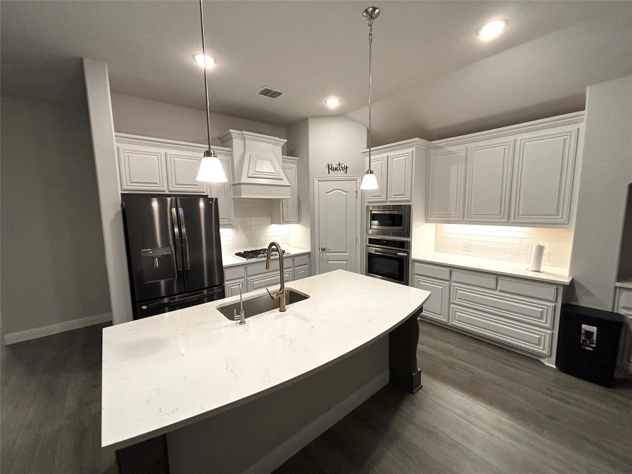 Kitchen with a kitchen island with sink, sink, tasteful backsplash, decorative light fixtures, and stainless steel appliances