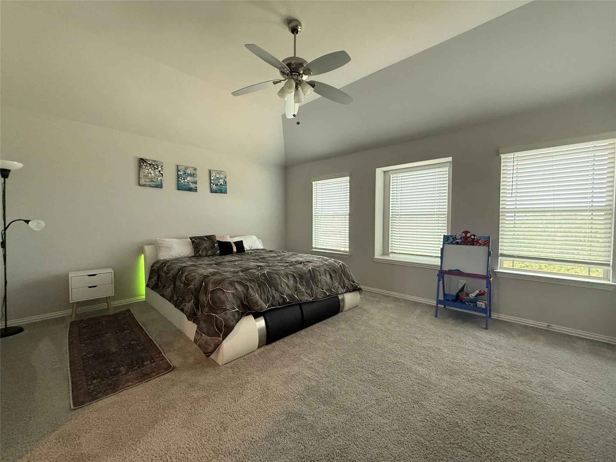 Carpeted bedroom with high ceiling, multiple windows, and ceiling fan