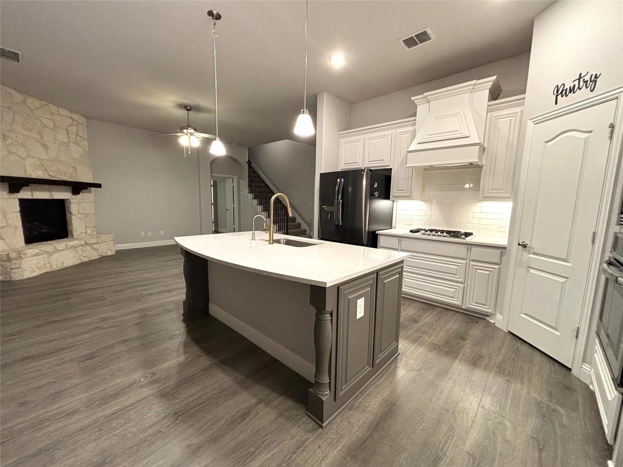 Kitchen with white cabinets, dark wood-type flooring, fridge with ice dispenser, and an island with sink