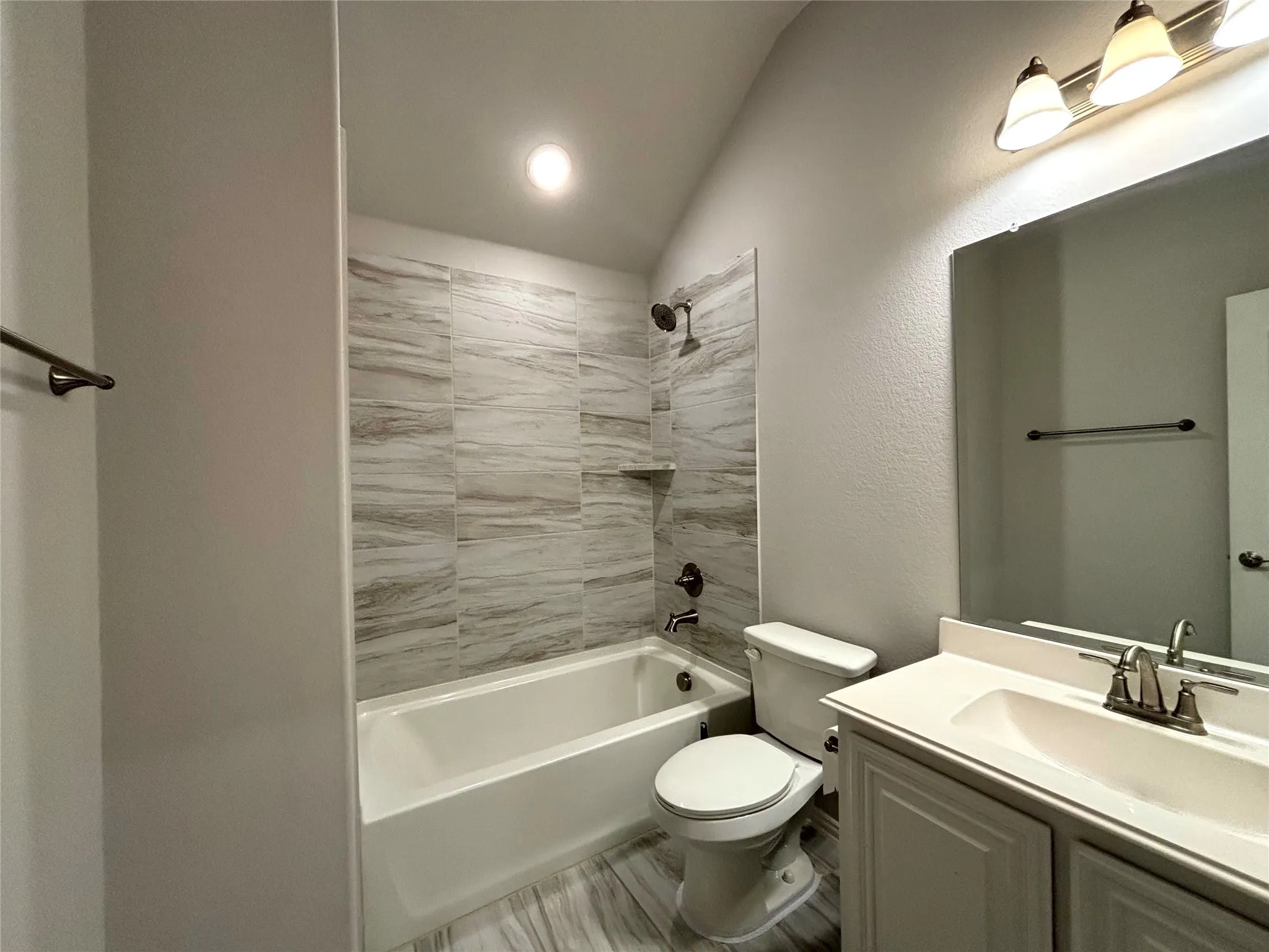 Full bathroom featuring toilet, vanity, tiled shower / bath combo, and vaulted ceiling