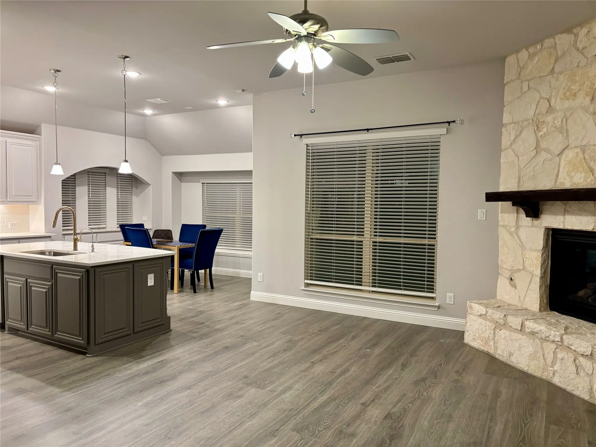 Kitchen with sink, pendant lighting, a kitchen island with sink, a fireplace, and hardwood / wood-style flooring