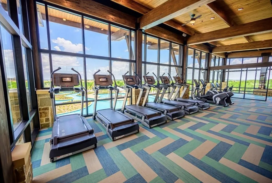 Community exercise room with wood ceiling, carpet flooring, and a wall of windows