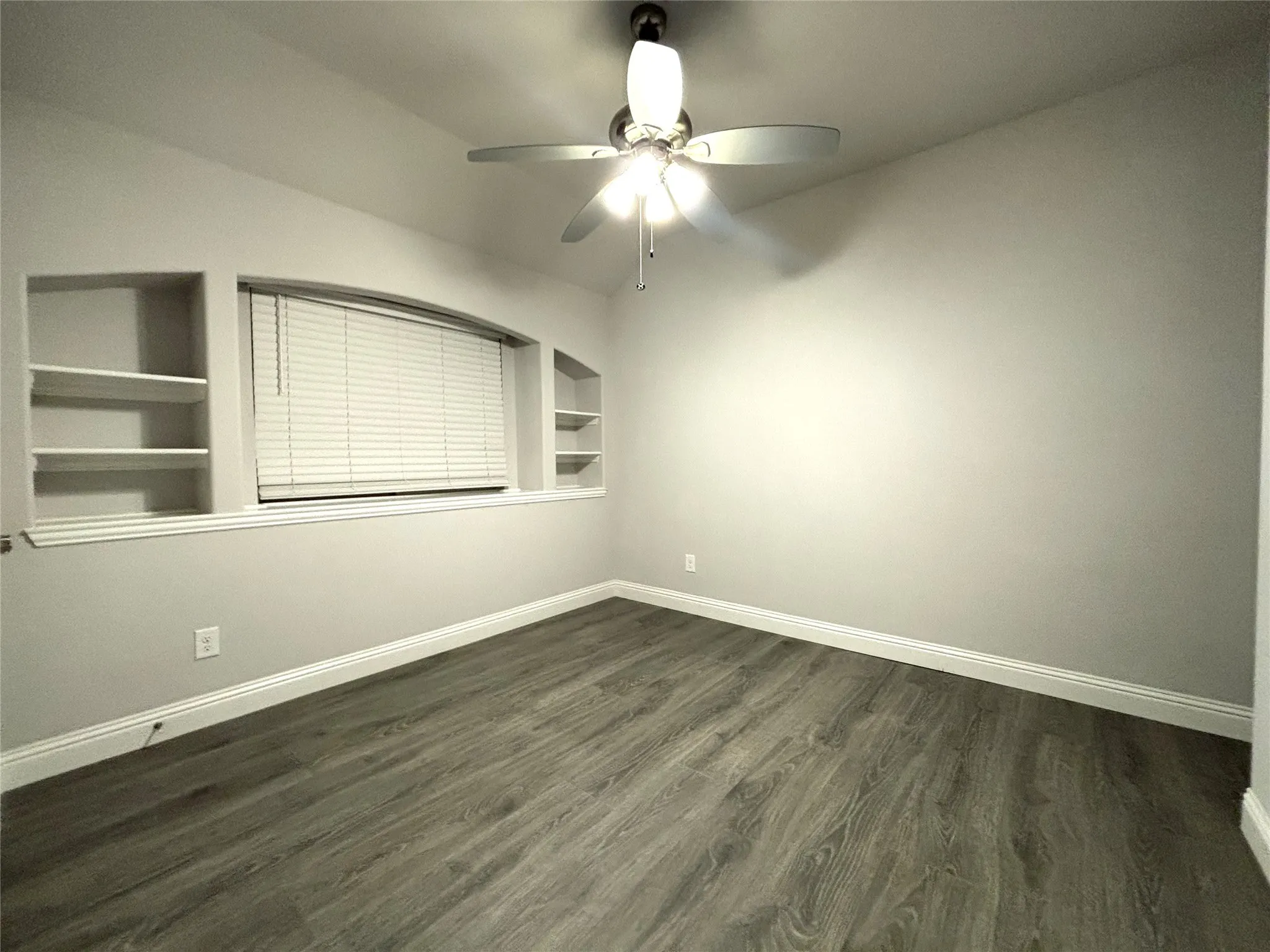 Unfurnished room featuring built in shelves, ceiling fan, and dark wood-type flooring