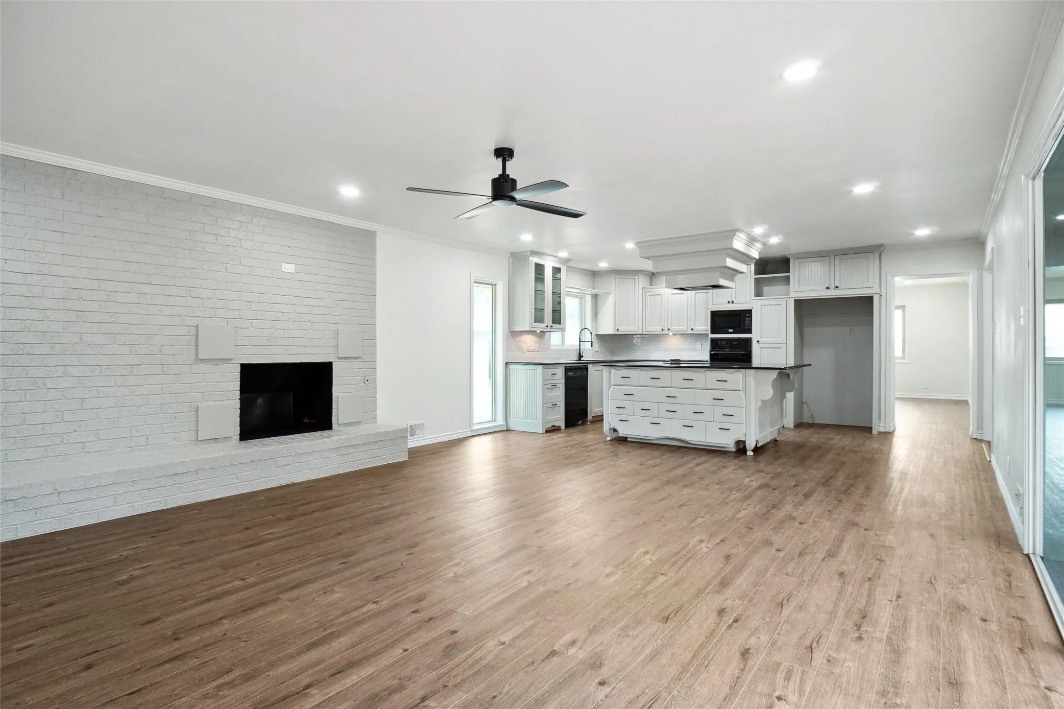 Kitchen with white cabinets, light hardwood / wood-style floors, black appliances, and crown molding