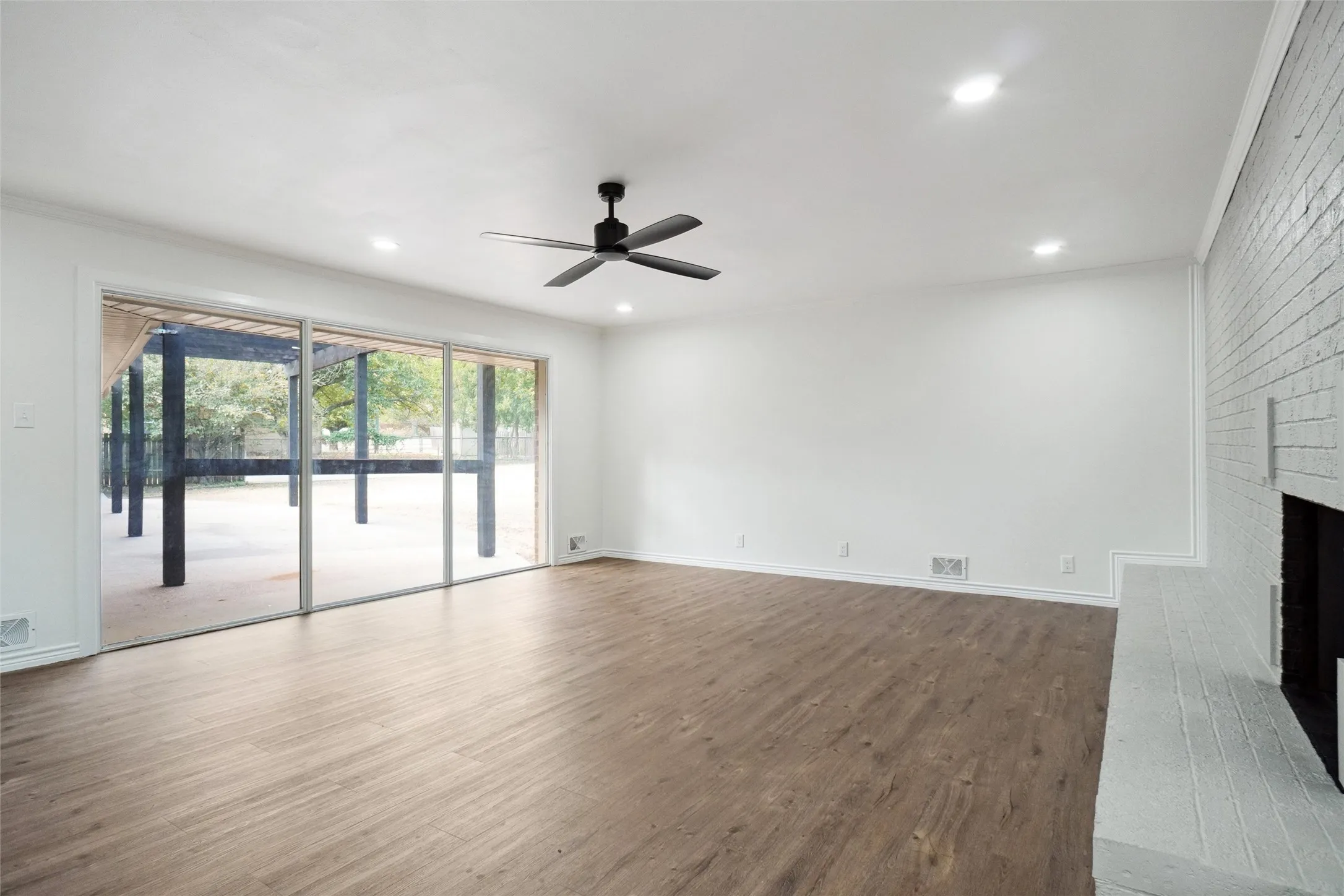 Unfurnished living room with a brick fireplace, ornamental molding, hardwood / wood-style flooring, and ceiling fan