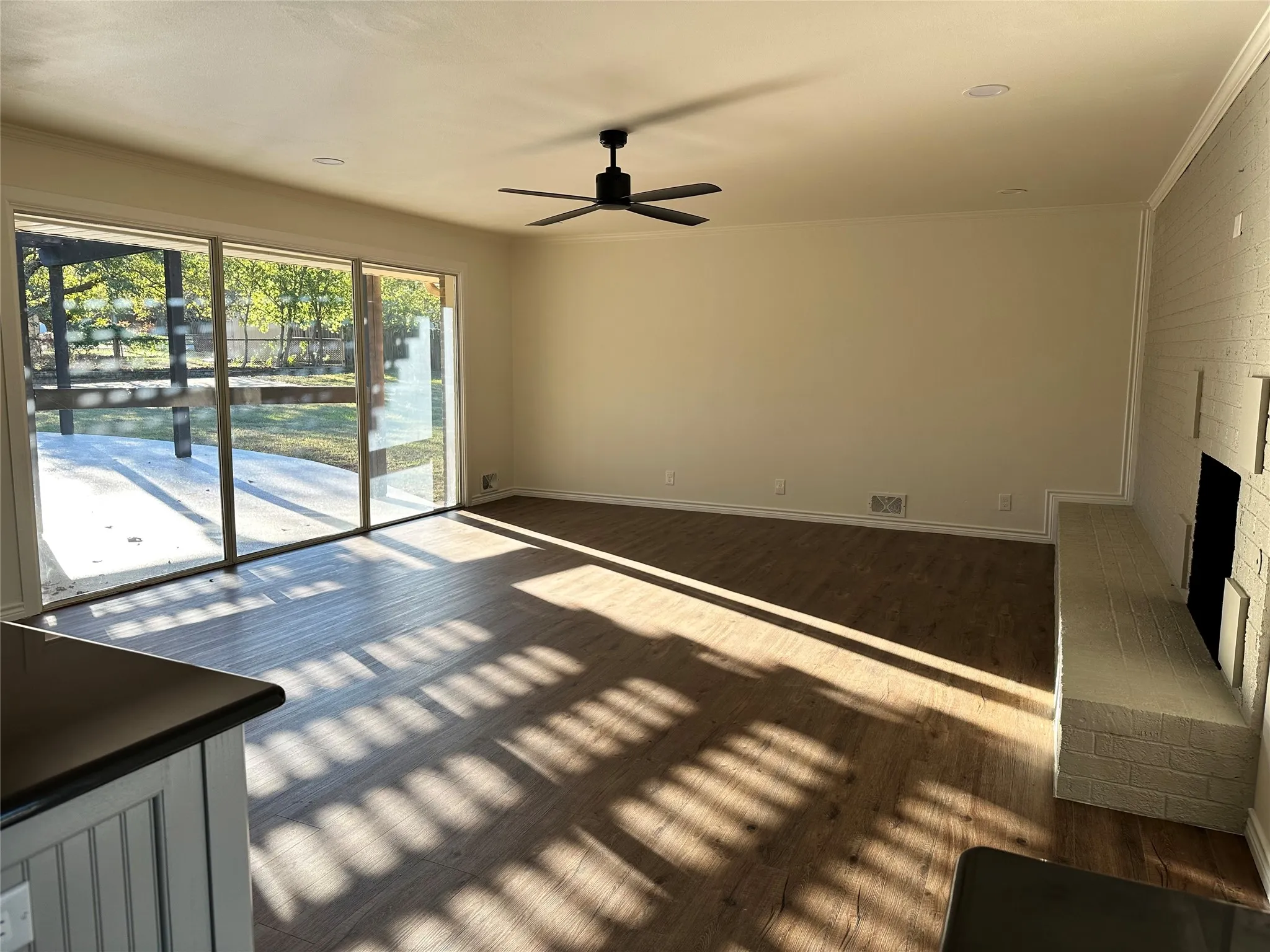 Unfurnished living room featuring ornamental molding, dark hardwood / wood-style floors, ceiling fan, a fireplace, and brick wall