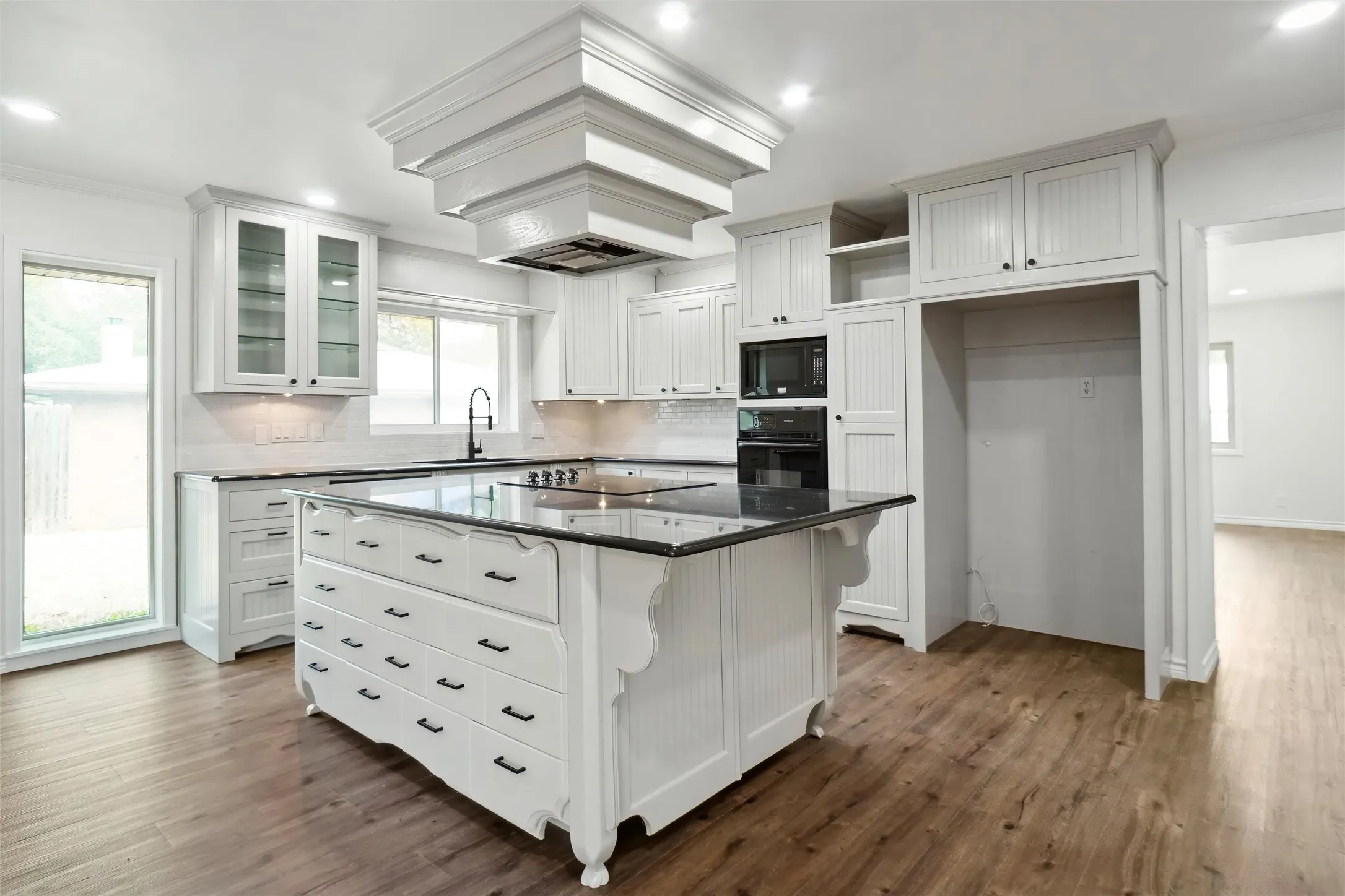 Kitchen with white cabinets, dark wood-type flooring, black appliances, and a kitchen island