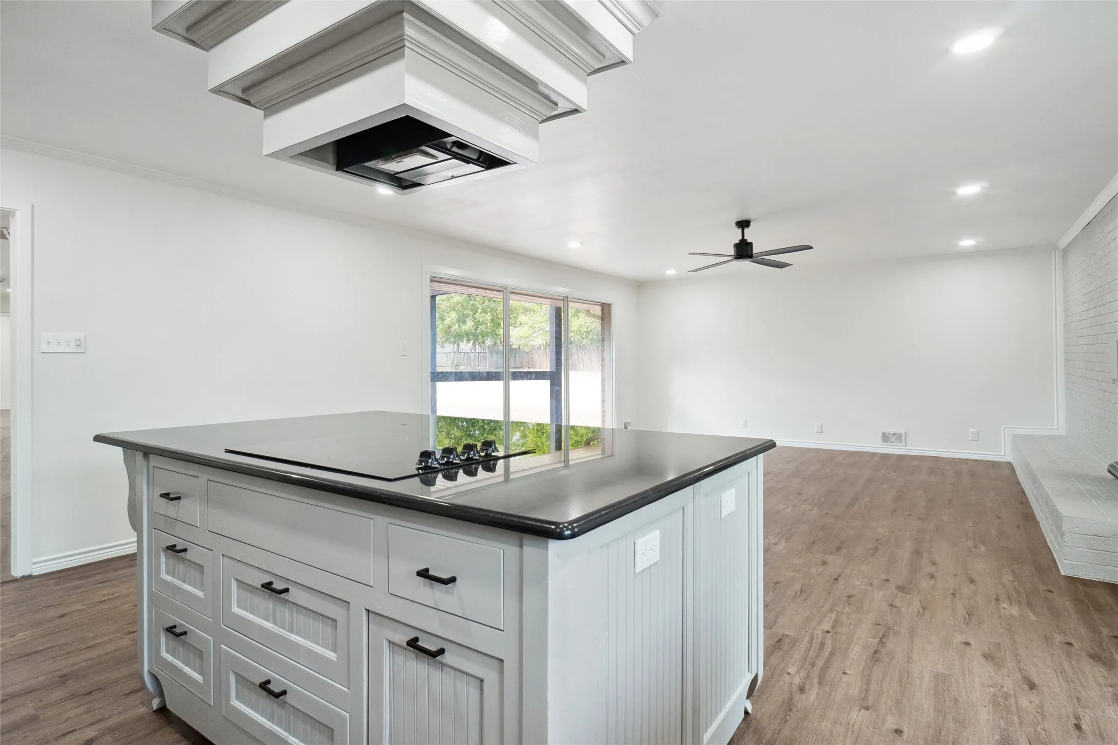 Kitchen featuring cooktop, crown molding, light wood-type flooring, ceiling fan, and a center island