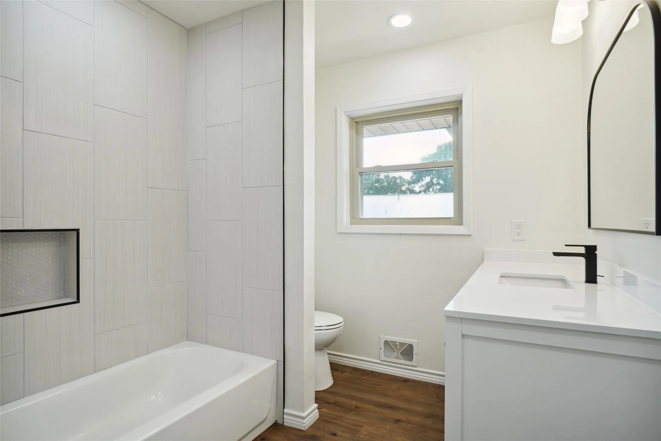 Full bathroom with tiled shower / bath combo, vanity, hardwood / wood-style flooring, and toilet