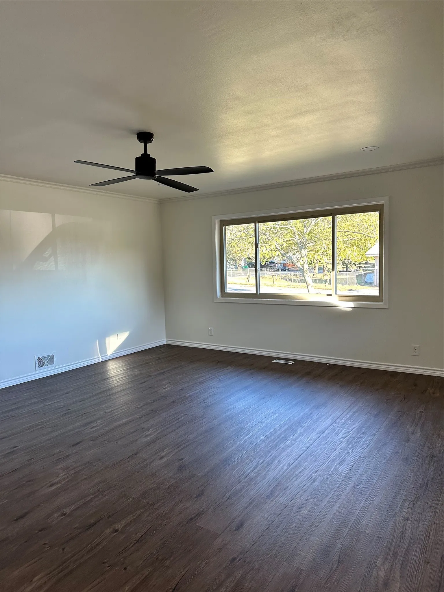 Empty room with dark wood-type flooring, ceiling fan, and plenty of natural light