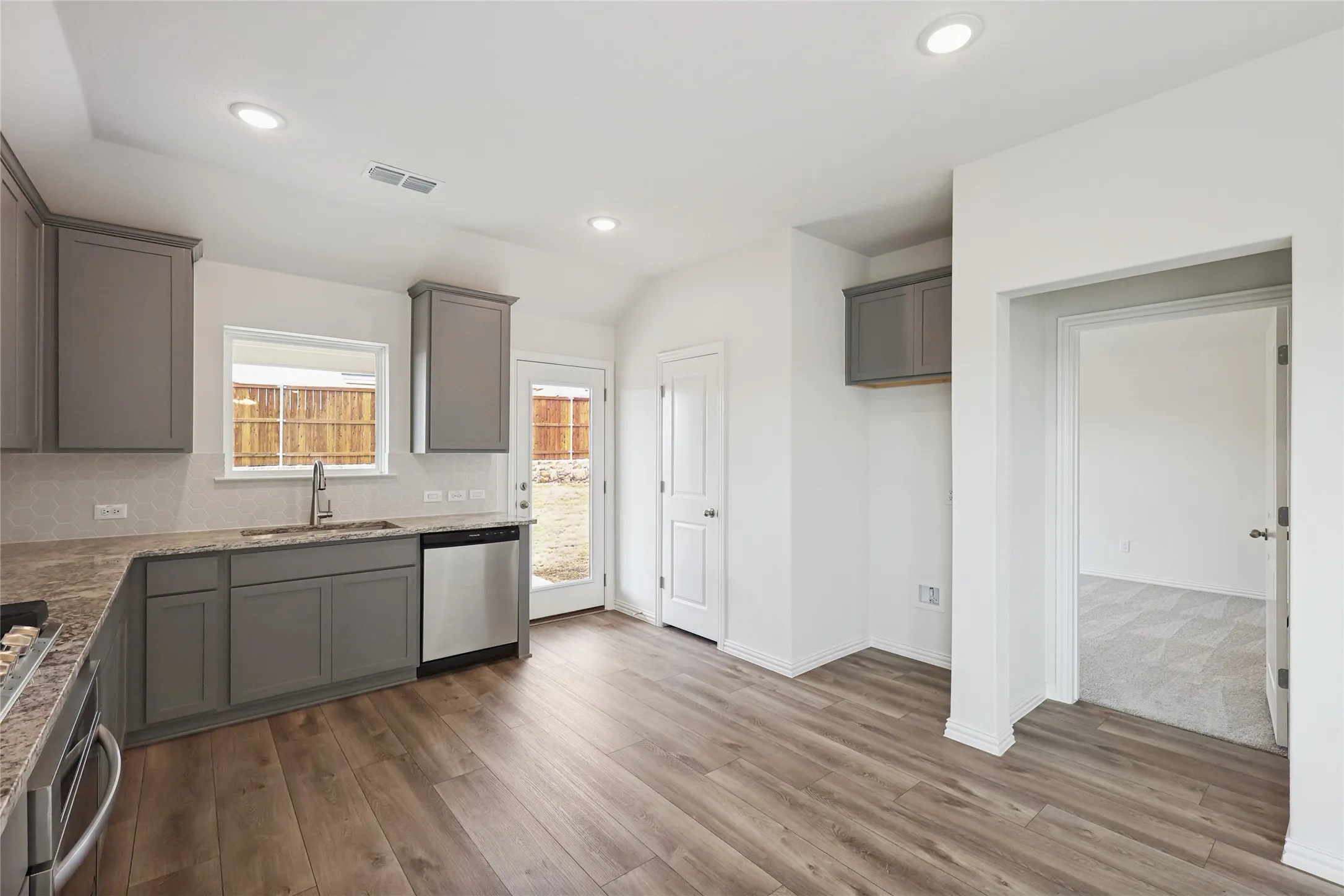 Kitchen with gray cabinets, wood-type flooring, sink, backsplash, and stainless steel dishwasher