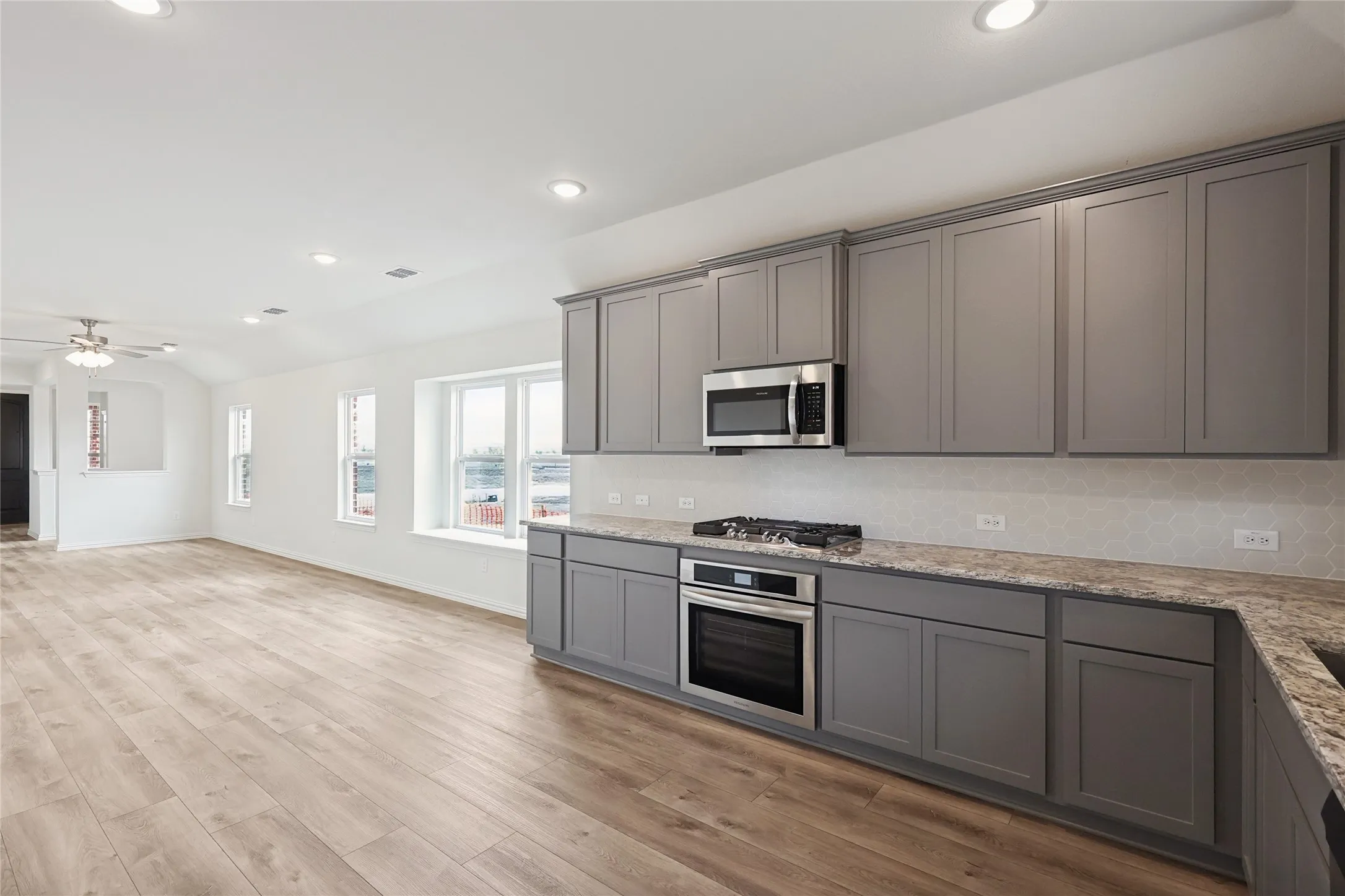 Kitchen with gray cabinets, wood-type flooring, sink, backsplash, and stainless steel dishwasher