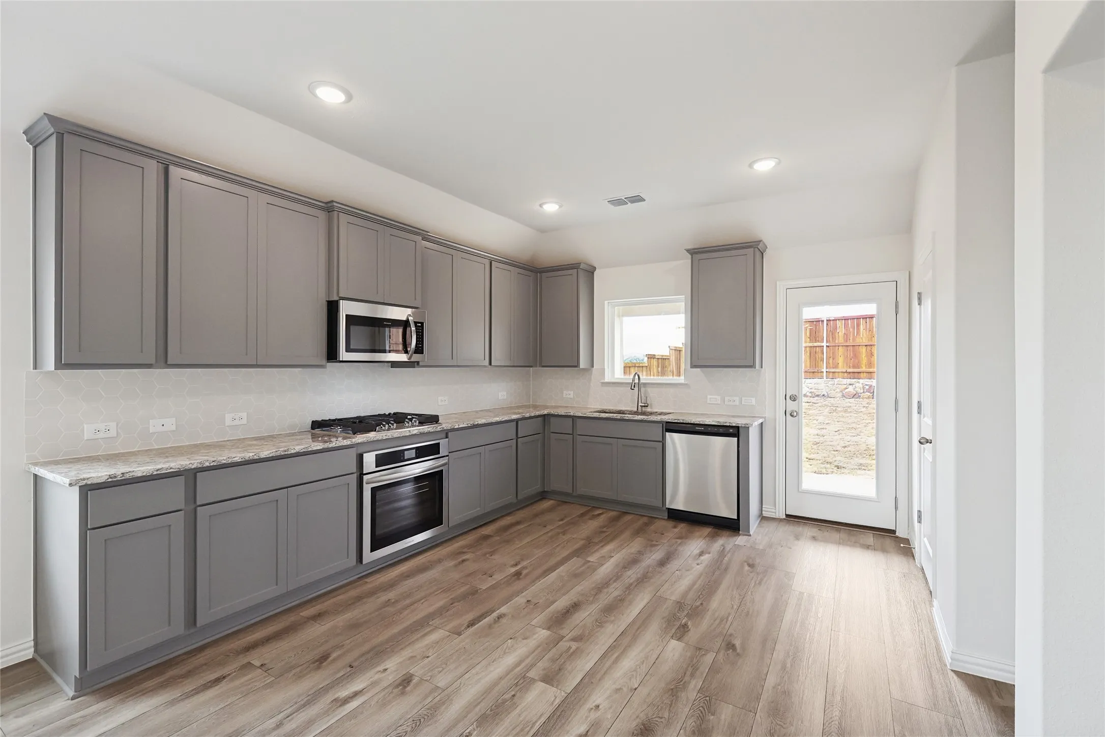 Kitchen with stainless steel appliances, sink, gray cabinetry, and backsplash