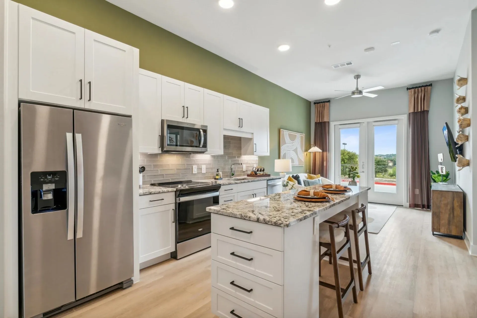 Kitchen with appliances with stainless steel finishes, light wood-type flooring, light stone counters, white cabinets, and a kitchen island