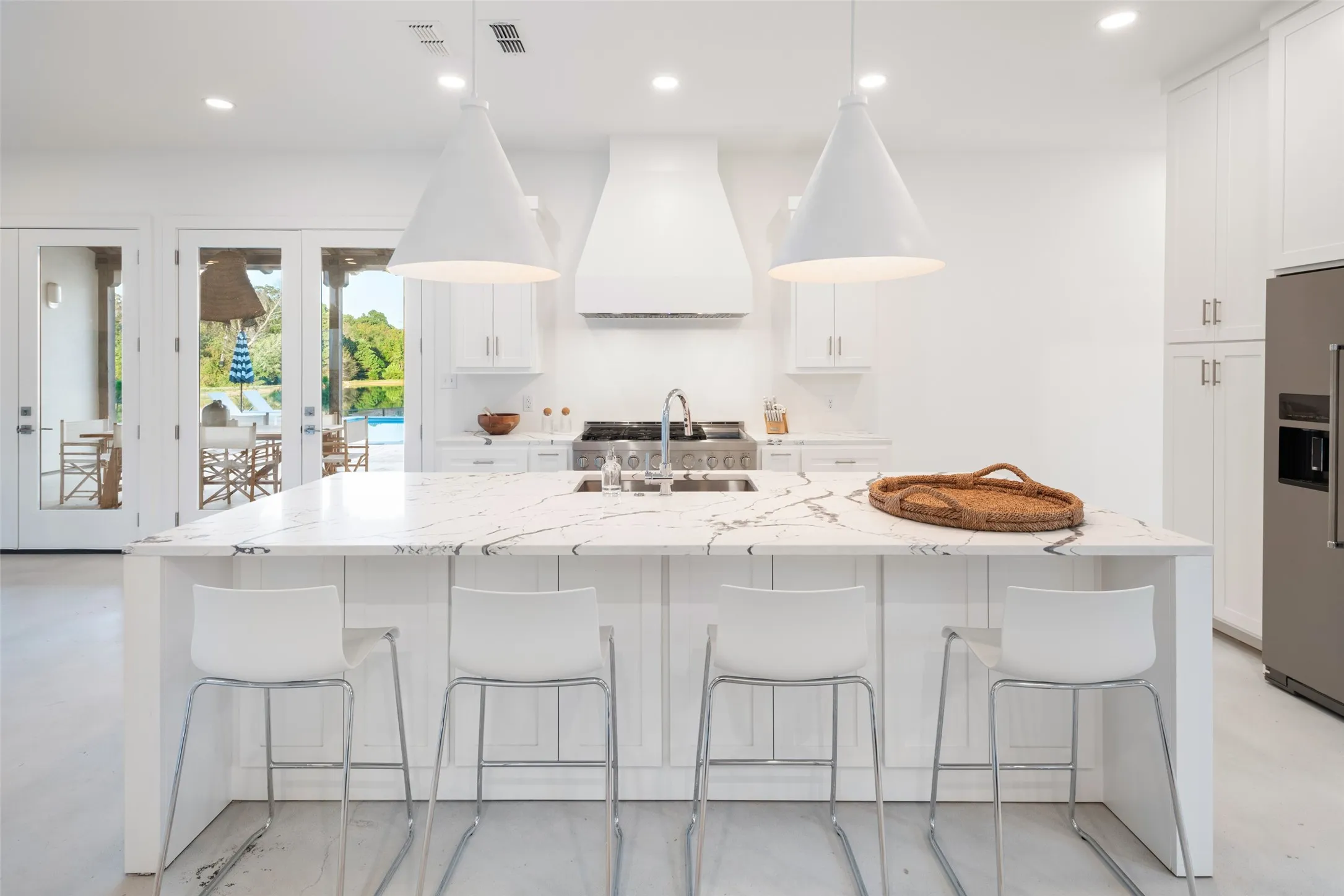 Kitchen with light stone counters, premium range hood, stainless steel refrigerator with ice dispenser, and an island with sink