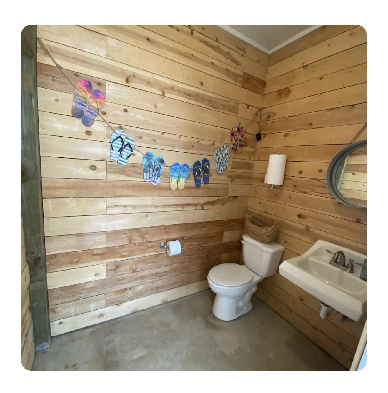 Bathroom with toilet, sink, wooden walls, and concrete floors