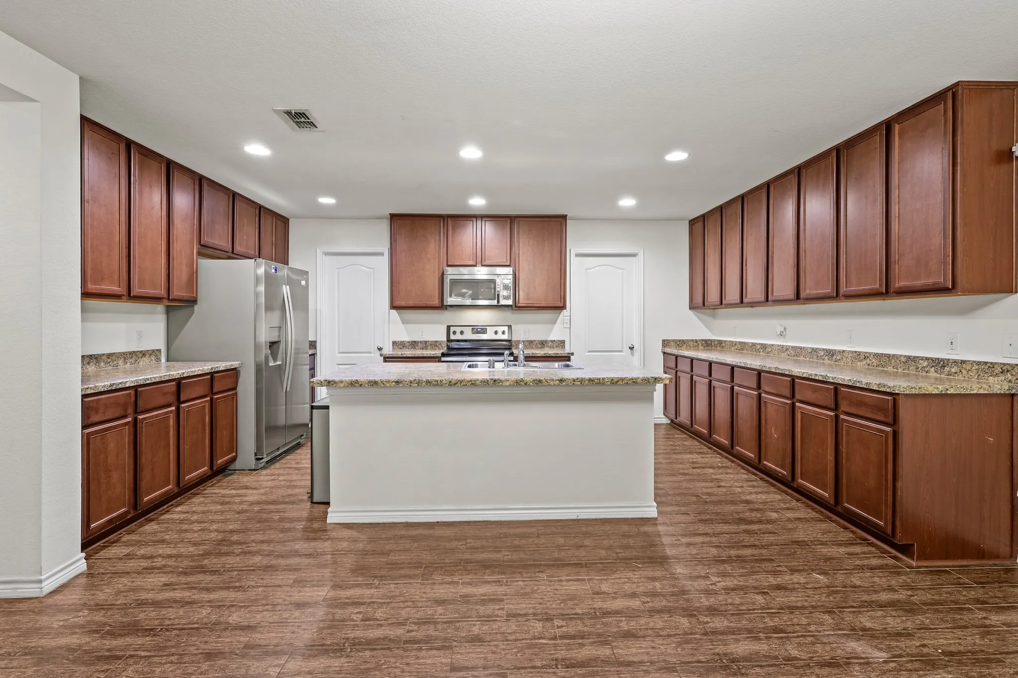Kitchen with dark hardwood / wood-style flooring, light stone countertops, stainless steel appliances, and an island with sink