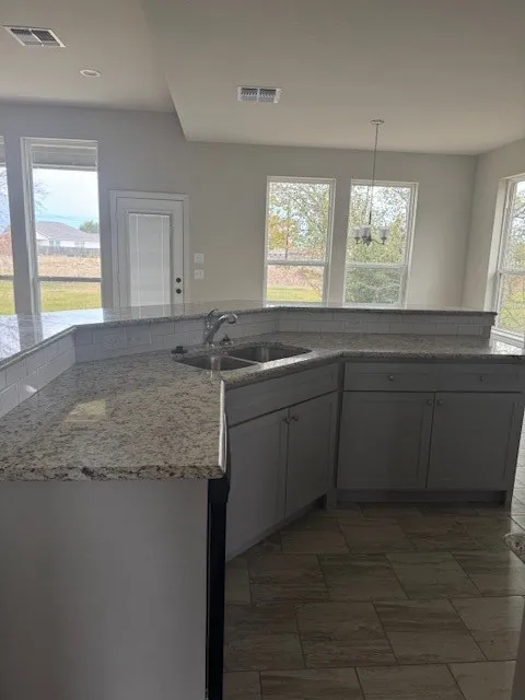 Kitchen featuring light stone countertops, a wealth of natural light, sink, and hanging light fixtures