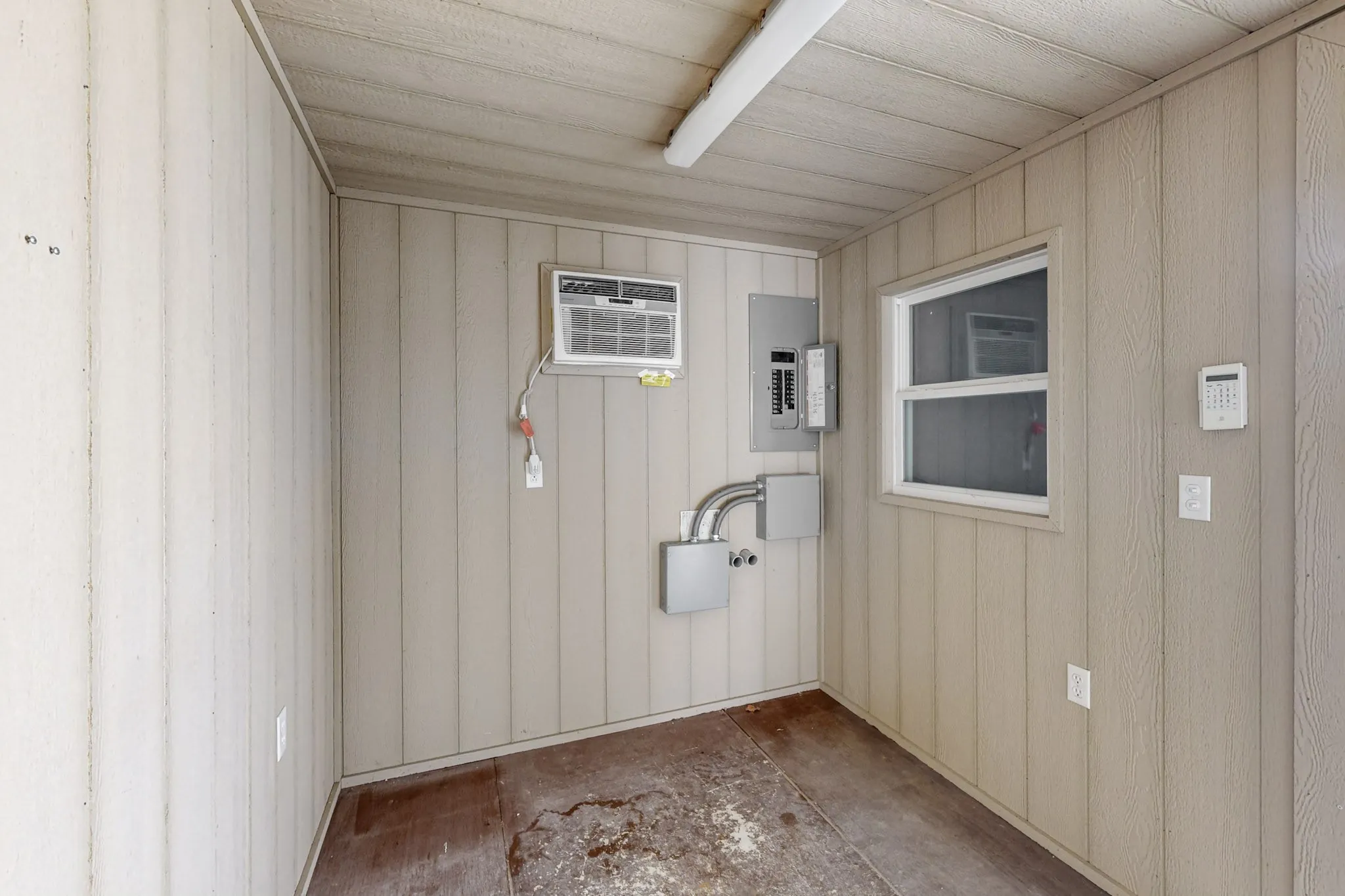 Unfurnished room with electric panel, a wall unit AC, and wooden walls