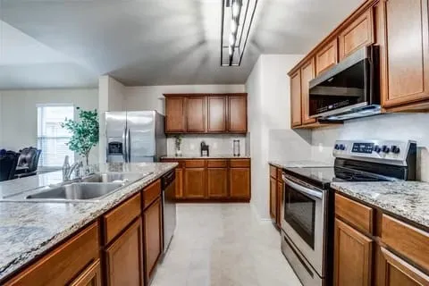 Kitchen with light stone counters, sink, and appliances with stainless steel finishes