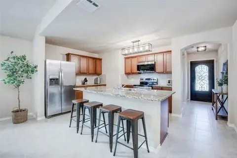 Kitchen with light stone counters, stainless steel appliances, a kitchen island, hanging light fixtures, and a breakfast bar area