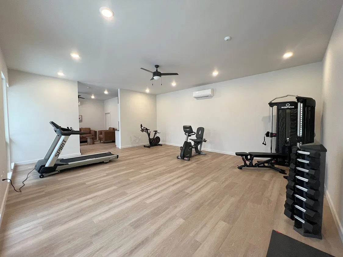 Workout room featuring ceiling fan, a wall unit AC, and light hardwood / wood-style flooring