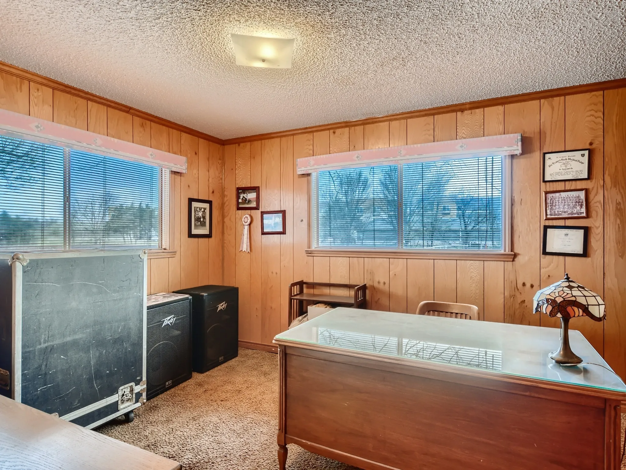 Bedroom with light carpet, a textured ceiling, and wooden walls