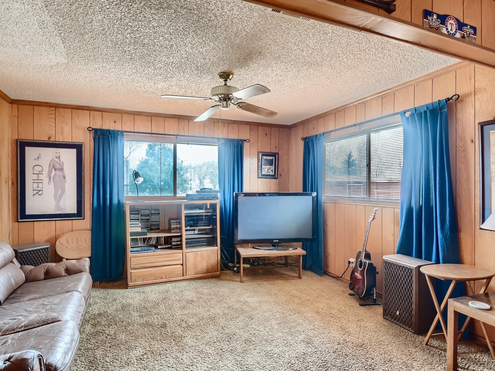 Living room featuring carpet flooring, a textured ceiling, ceiling fan, and wood walls